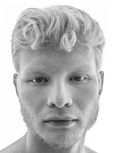Black-and-white high-key portrait of a young man with pale curly hair and light stubble