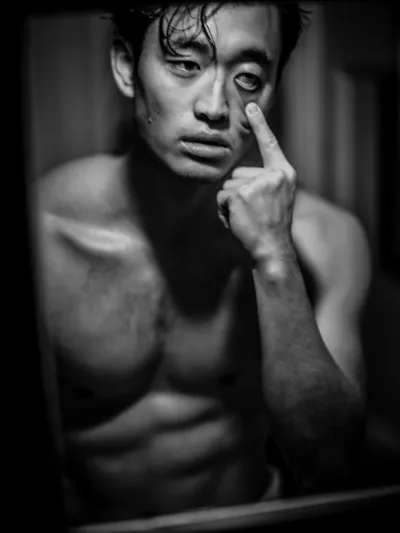 Dramatic black-and-white portrait of a shirtless man with wet hair, finger to his cheek