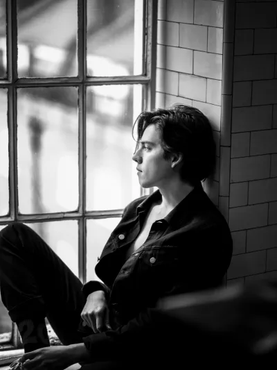 Black-and-white profile of a young man in a denim jacket by a large industrial window