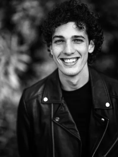 Black-and-white portrait of a smiling young man with curly hair in a leather biker jacket