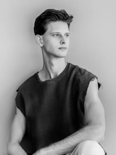Black-and-white profile of a young man in a distressed sleeveless top against a plain wall