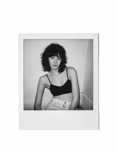 Black-and-white instant-film portrait of a woman in a black bralette and white jeans