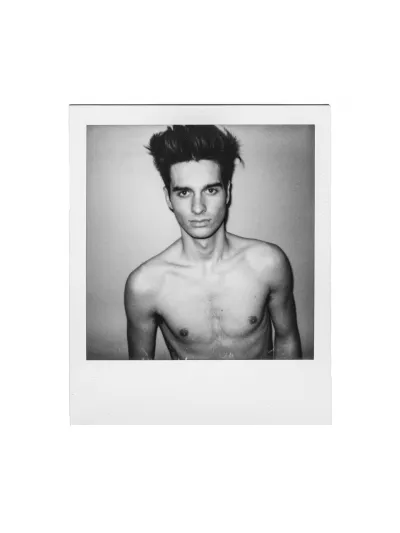 Black-and-white instant-film portrait of a shirtless young man with spiky hair
