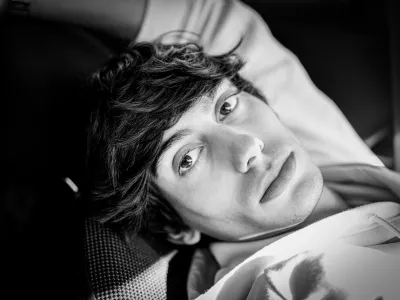 Black-and-white close portrait of a young man lying down and looking up at the camera