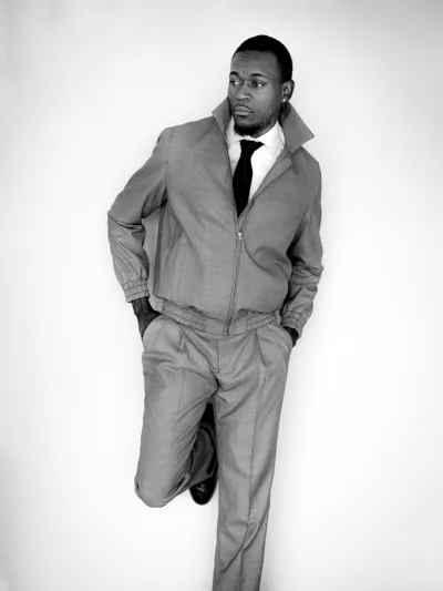 Black-and-white full-length portrait of a man in a grey checked tracksuit against a white wall