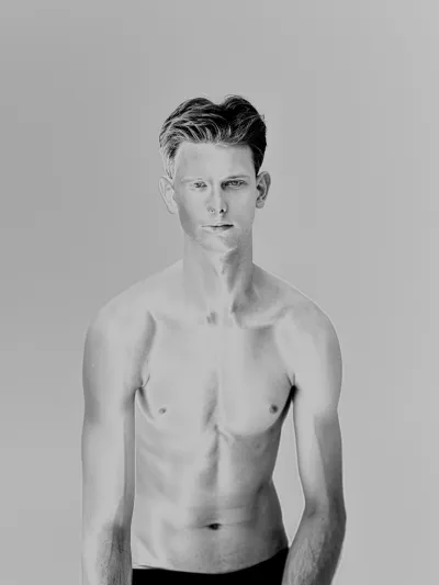 Black-and-white studio portrait of a slim shirtless young man on a grey background