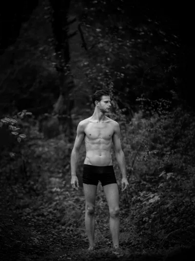 Black-and-white forest portrait of a shirtless man in briefs on a woodland path