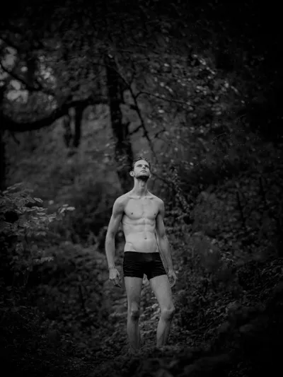 Black-and-white forest portrait of a shirtless man in briefs looking upward