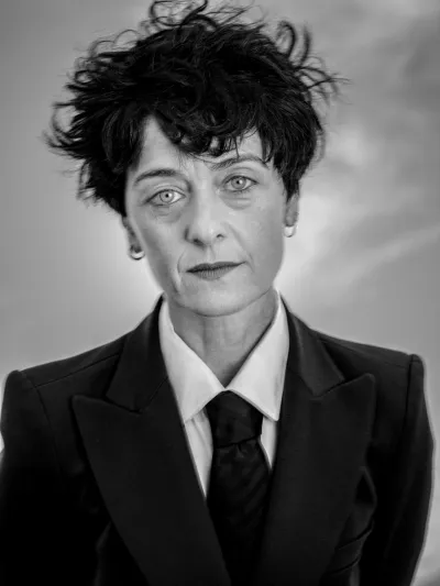 Black-and-white studio portrait of a woman in a black suit, shirt and tie