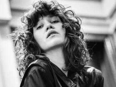 Black-and-white low-angle portrait of a woman with curly hair in a black leather jacket