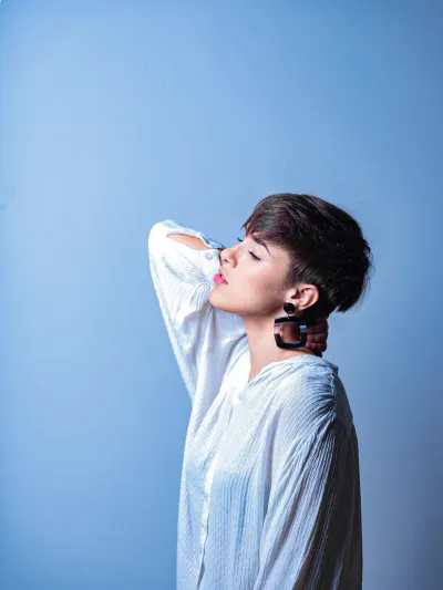 Color portrait of a woman with a dark pixie cut and large earring on a blue background