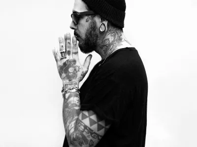 Black-and-white profile of a heavily tattooed man in a beanie and sunglasses
