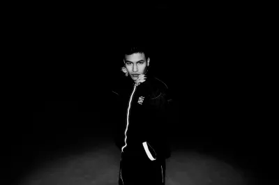 Dramatic black-and-white portrait of a young man in a striped track jacket in darkness