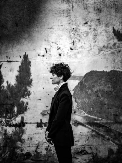 Dramatic black-and-white portrait of a person in a black blazer before a weathered mural wall