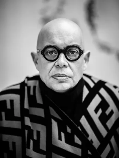 Black-and-white portrait of a bald man in round glasses and a monogram-patterned sweater